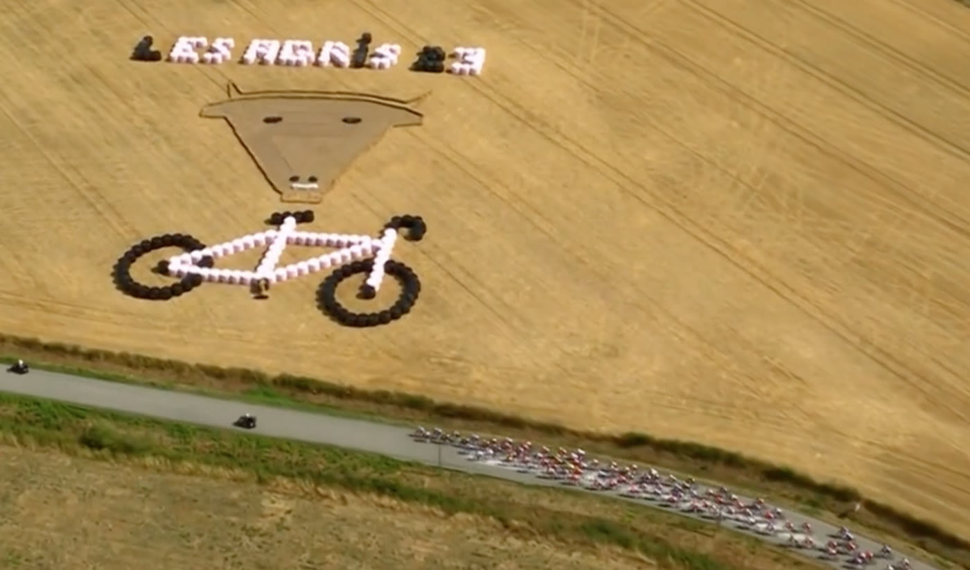 Vue aérienne du peloton du Tour de France Femmes longeant un champ décoré d'un vélo en bottes de paille